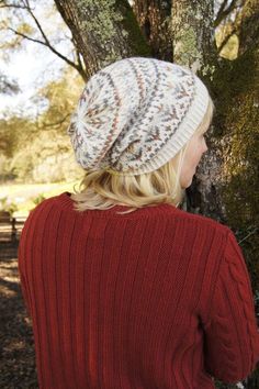 a woman standing next to a tree wearing a red sweater and a white knitted hat