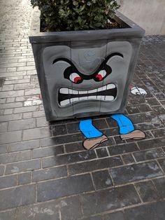 a potted planter with an angry face painted on the ground next to a brick sidewalk