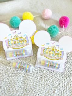 two mickey mouse shaped erasers sitting on top of a white blanket next to pom - poms