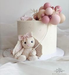 a white cake topped with a teddy bear and balloons