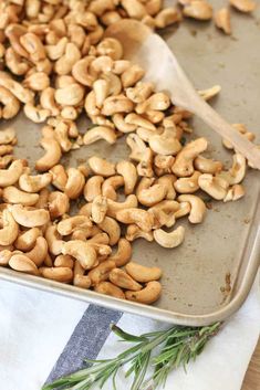 roasted cashews on a baking sheet with a wooden spoon and rosemary sprig