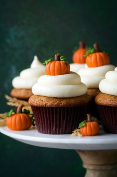 cupcakes with white frosting and mini pumpkins are on a cake plate