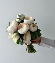 a bouquet of white roses being held by someone's hand on a gray background