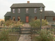 an old house with a gate and light post in the foreground, surrounded by shrubbery