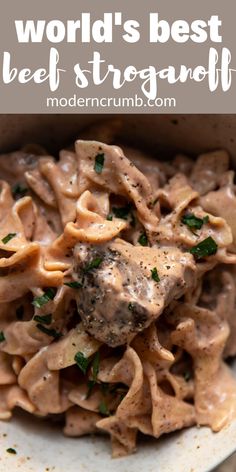 a white bowl filled with pasta and meat covered in gravy on top of a wooden table