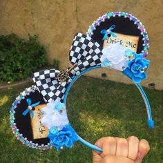 a hand holding up a mickey mouse ears headband with flowers and blue beads on it