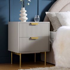 a white and gold chest of drawers next to a bed with blue walls in the background