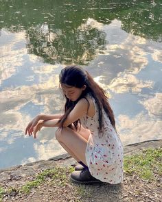 a young woman sitting on the ground next to a body of water