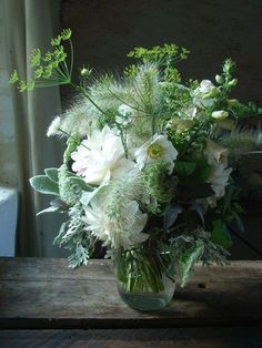 a vase filled with lots of white flowers on top of a wooden table next to a window