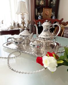 a silver tea set on a tray with a rose in the middle and pearls around it