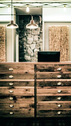 a wooden dresser sitting in front of a stone wall with two lamps hanging above it