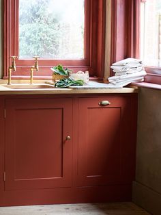 a kitchen with red painted cabinets and a window in the corner that looks out onto trees