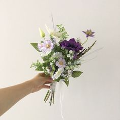 a bouquet of flowers being held by someone's hand on a white wall background