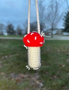 a crocheted red mushroom hanging from a string in front of a grassy field