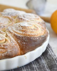 an orange and cinnamon roll on a white plate next to some powdered sugar sprinkles