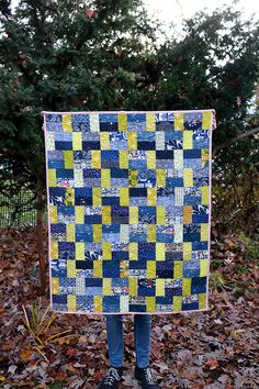 a person standing in leaves holding up a blue and yellow quilt