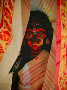 a black mask with red and yellow designs on it's face sitting in the corner of a bed