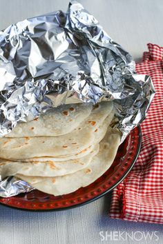 a plate filled with tortillas wrapped in aluminum foil on top of a red and white checkered napkin