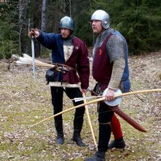 two men dressed in medieval clothing holding spears and arrows