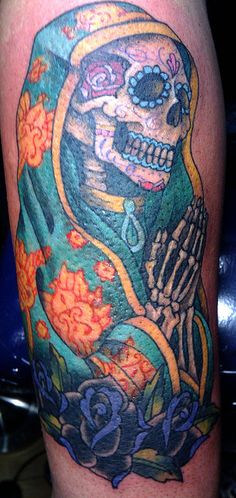 a tattoo with a skeleton and flowers on the thigh, in front of a blue chair