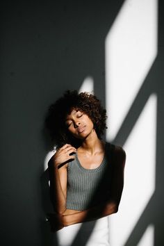 a woman standing in front of a white wall with her hands on her hips and looking at the camera