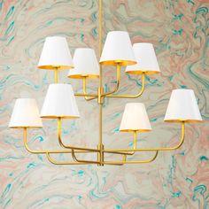 a gold chandelier with white lamps hanging from it's sides in front of a marble wall