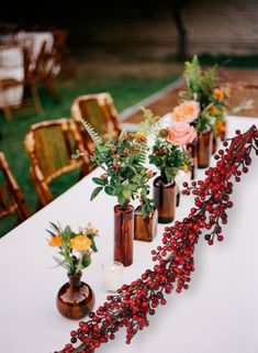 several vases filled with flowers sitting on top of a white table covered in greenery