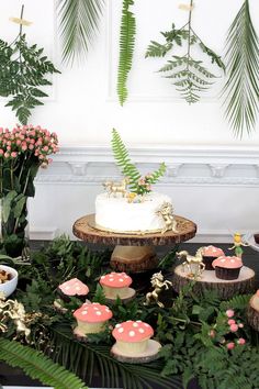 a table topped with cupcakes covered in frosting and surrounded by greenery