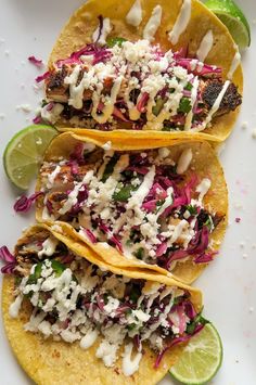 three tacos on a plate with lime wedges and shredded red cabbage slaw