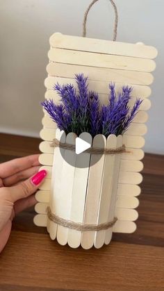 a hand holding a wooden box with purple flowers in it