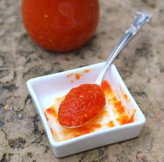 a small square white bowl filled with sauce next to an orange on the counter top