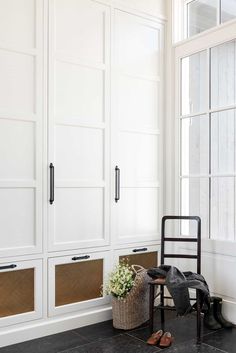 a room with some white cabinets and a chair in front of the window, next to a plant