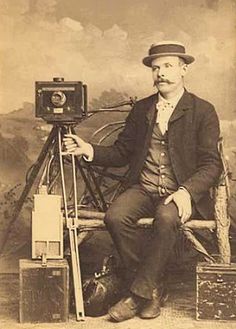 an old time photo of a man sitting in front of a camera with a tripod