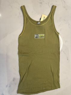 Cotton stretch knit tank top in green. 70s yellow rib knit crewneck and armscye. 57YE Naval Air Station Flight Experience logo at front. Size fits small Fitted 90s Crew Neck Tank Top, Retro Ribbed Summer Top, Retro Ribbed Tops For Summer, Retro Fitted Crew Neck Tank Top, Fitted Retro Crew Neck Tank Top, Vintage Ribbed Cotton Tops, Fitted Olive Sleeveless Top, Fitted Sleeveless Olive Top, Fitted Green 90s Tops