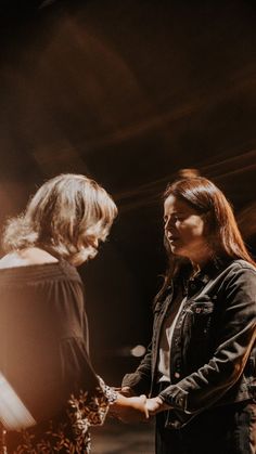 two women standing next to each other in front of a dark background with light coming through them