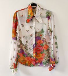 RARE FIND A fabulous early 1970s shirt from Jeff Banks, in bright floral print pattern.   Lightweight material in white with orange, yellow, pink and green floral print throughout. Fastens to the front with double buttons, and three buttons at each cuff with a gathered balloon sleeve.  Slim fit with a rounded hem to front and back. Fantastic dog ear collar detail for a classic vintage style. Looks amazing worn with blue denim flares and platform sandals! Material: 75% Acetate / 25% Nylon Conditi White Retro Print Shirt For Spring, Retro Multicolor Print Shirt For Spring, White Shirt With Retro Print For Spring, Retro White Shirt With Floral Print, White Retro Shirt With Floral Print, White Retro Floral Print Shirt, Vintage White Blouse With Floral Print, Vintage White Floral Print Blouse, Retro Multicolor Floral Print Blouse