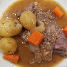 a white plate topped with meat, potatoes and carrots next to gravy