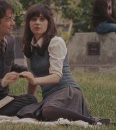 a man and woman sitting on top of a grass covered field next to each other