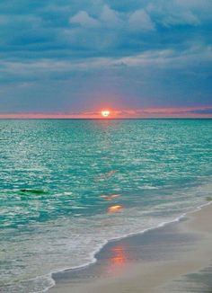 the sun is setting over the ocean with clouds in the sky and water on the beach