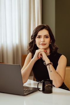 a woman sitting at a table in front of a laptop computer with her hand on her chin