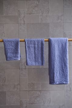 three blue towels hanging on a clothes line in a bathroom with tile walls and floor