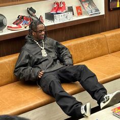 a man with dreadlocks sitting on a bench in a shoe store looking at his cell phone