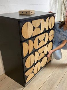 a woman kneeling down next to a black and wood cabinet with circles on it's sides