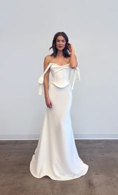 a woman in a white dress posing for the camera with her hand on her head