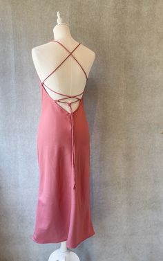 "Slip midi dress with adjustable criss cross back straps featuring a cowl neck in pink berry color. Mid calf length. Lightweight non-stretchy fabric. Model is (172 cm - 5'8\") and (53 kg - 117 lbs) and is wearing size S Handmade in Bali Composition: 100% Viscose" Formal Spring Backless Dress With Ruched Back, Spring Formal Backless Dress With Ruched Back, Spring Halter Neck Midi Dress With Crisscross Straps, Spring Midi Dress With Halter Neck And Crisscross Straps, Midi Length Dress With Crisscross Straps For Date Night, Date Night Midi Dress With Crisscross Straps, Midi Dress With Crisscross Straps For Date Night, Elegant Backless Dress With Wrap-around Straps, Spring Satin Backless Dress With Lace-up Back