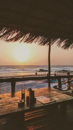 the sun is setting over an ocean with boats in the water and people sitting at tables under umbrellas