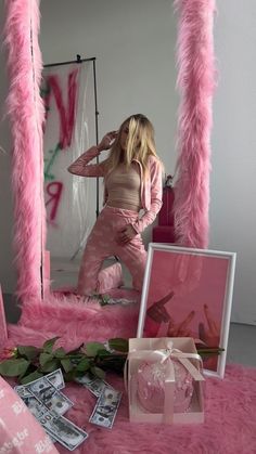 a woman standing in front of a mirror with pink feathers on the floor and money