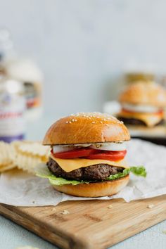 a hamburger sitting on top of a wooden cutting board next to a pile of chips