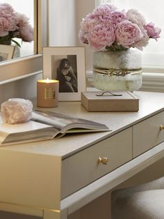 pink flowers in a vase sitting on a desk next to a mirror and candle holder