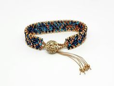 This beautiful beaded macrame bracelet is made by hand, in a mix of peacock blue, aqua, gold and copper Czech glass beads.  It has a golden filigreed button and macrame loop clasp. It is available in a flax beige or dark peacock color macrame cording. Please choose cord color and size in variations.  There are strands dangling from the clasp.  If you prefer not to have the dangling strands, please message me first, before ordering. SIZE & DETAILS: > 6, 6 1/2, 7, 7 1/4, 7 1/2 or 8     inch hand w Gold Macrame Beaded Bracelets, Macrame Wave, Macrame Unique, Purple Beaded Bracelets, Blossom Bracelet, Geometric Arrow, Jewelry Making Business, Golden Copper, Wave Bracelet